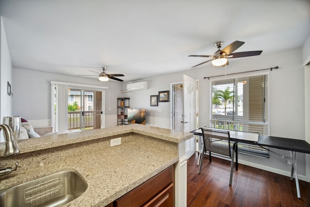 kitchen with dark wood-type flooring, an AC wall unit, sink, ceiling fan, and light stone counters