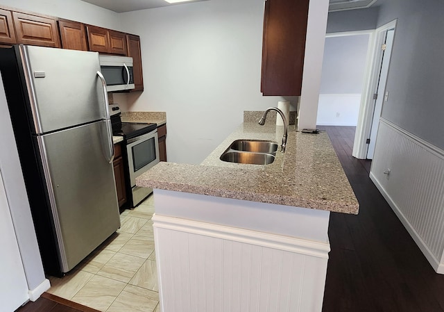 kitchen with kitchen peninsula, light stone counters, sink, and stainless steel appliances