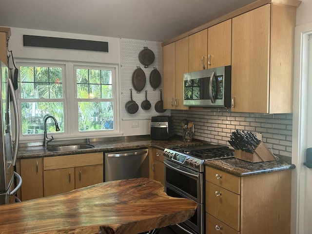 kitchen featuring appliances with stainless steel finishes, decorative backsplash, light brown cabinets, dark stone countertops, and sink