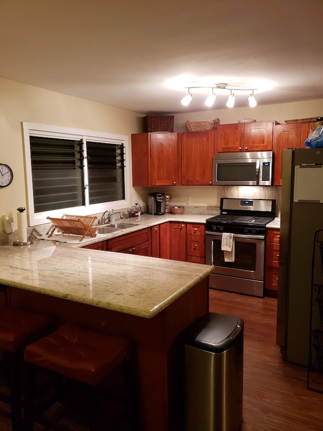 kitchen with dark wood-type flooring, sink, appliances with stainless steel finishes, and kitchen peninsula