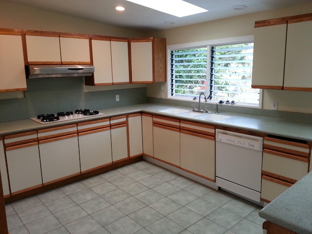 kitchen featuring light tile patterned floors, backsplash, white appliances, vaulted ceiling with skylight, and sink