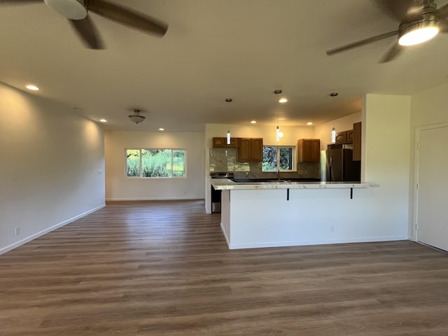 kitchen with kitchen peninsula, black fridge, dark hardwood / wood-style flooring, a breakfast bar area, and stainless steel range with electric stovetop