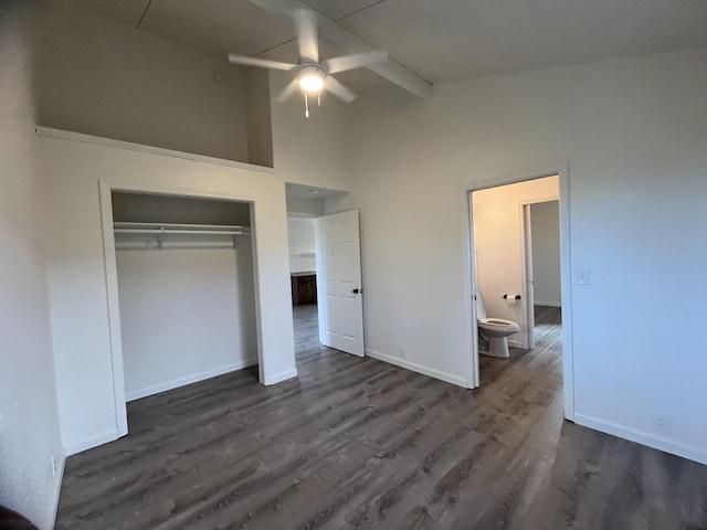 unfurnished bedroom with ensuite bath, ceiling fan, dark wood-type flooring, beamed ceiling, and a closet