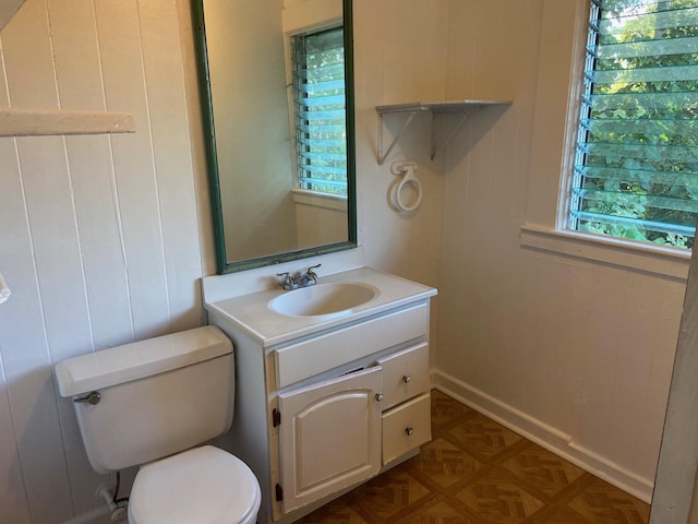 bathroom with parquet flooring, vanity, wood walls, and toilet