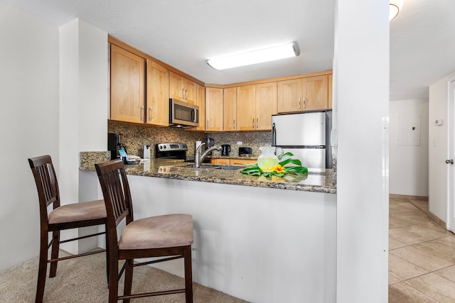 kitchen featuring stainless steel appliances, tasteful backsplash, dark stone countertops, light brown cabinetry, and light tile patterned flooring