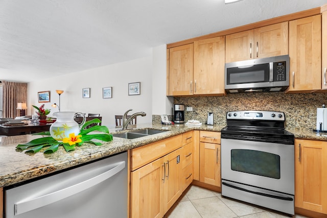 kitchen with appliances with stainless steel finishes, backsplash, light stone counters, sink, and light tile patterned floors