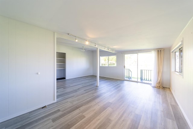 empty room featuring wooden walls, light hardwood / wood-style floors, and rail lighting