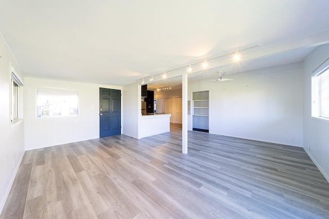 unfurnished living room with track lighting, a healthy amount of sunlight, and light hardwood / wood-style floors