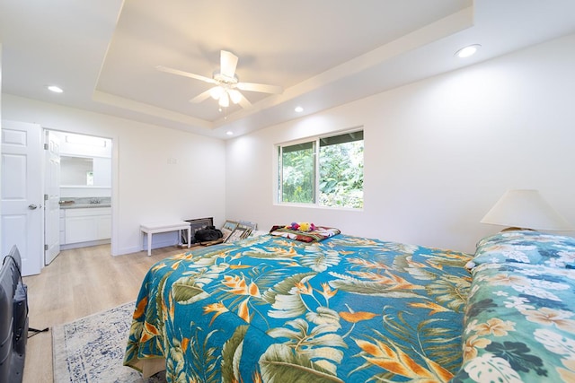 bedroom with light hardwood / wood-style floors, connected bathroom, ceiling fan, and a tray ceiling