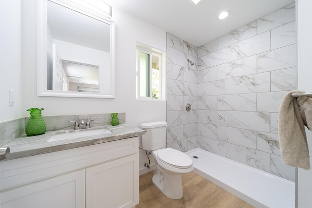 bathroom with hardwood / wood-style flooring, vanity, toilet, and a tile shower