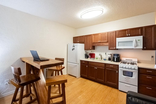 kitchen featuring a textured ceiling, sink, light hardwood / wood-style floors, and white appliances