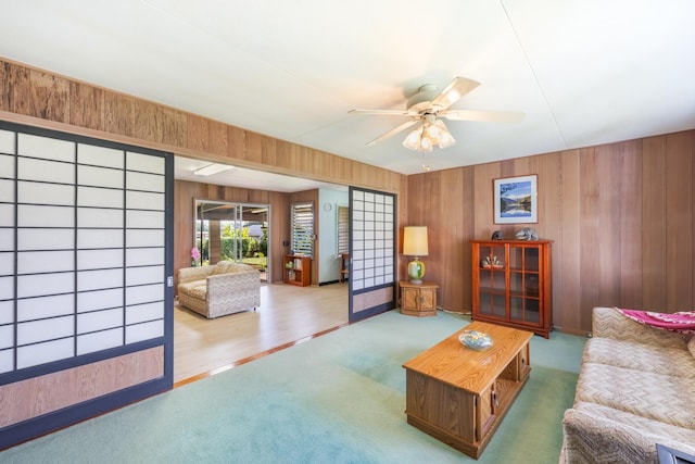 living room with carpet floors, ceiling fan, and wood walls