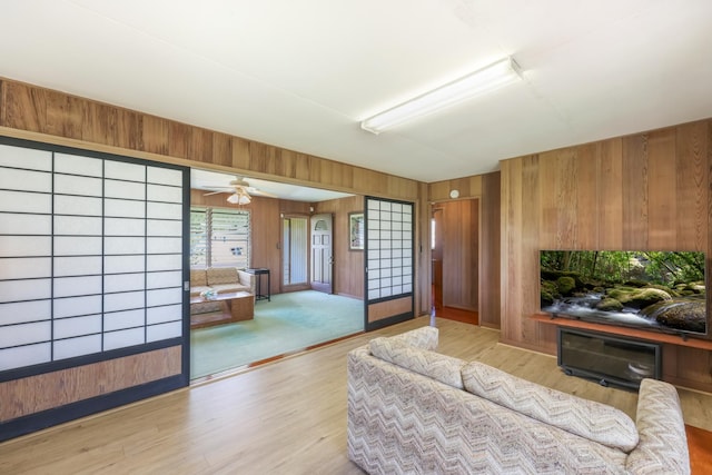 living room featuring light hardwood / wood-style flooring, ceiling fan, and wooden walls