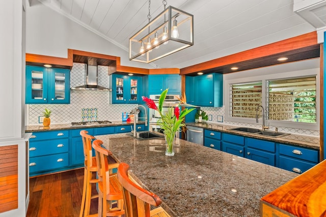 kitchen featuring pendant lighting, blue cabinets, sink, vaulted ceiling, and wall chimney exhaust hood