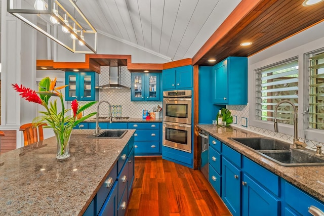 kitchen with sink, wooden ceiling, stainless steel double oven, wall chimney range hood, and decorative light fixtures