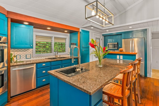 kitchen featuring stainless steel appliances, vaulted ceiling, sink, a center island with sink, and hanging light fixtures