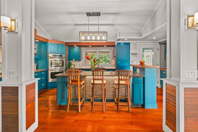 bar featuring lofted ceiling, crown molding, blue cabinetry, decorative light fixtures, and stainless steel double oven