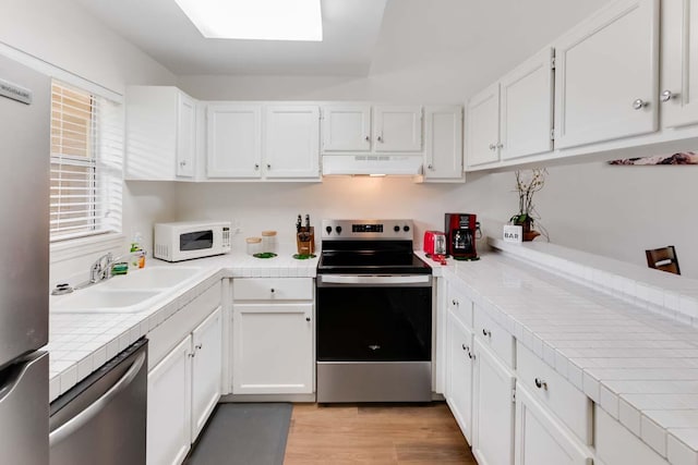 kitchen with appliances with stainless steel finishes, sink, white cabinets, light hardwood / wood-style floors, and tile counters