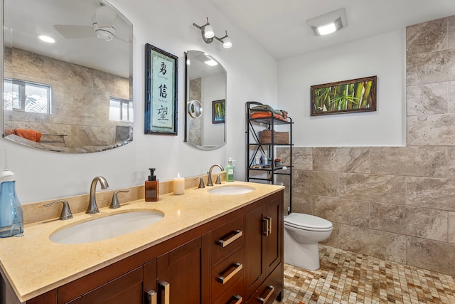 bathroom with ceiling fan, walk in shower, toilet, vanity, and tile walls