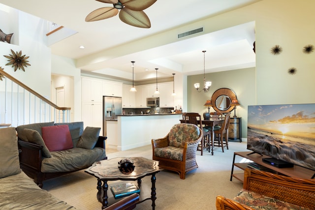 carpeted living room with ceiling fan with notable chandelier and a tray ceiling