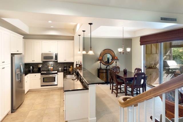 kitchen featuring white cabinets, stainless steel appliances, a raised ceiling, and hanging light fixtures