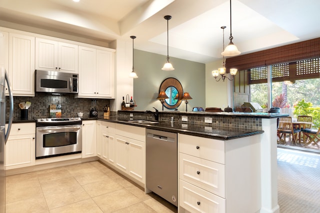 kitchen with a raised ceiling, sink, decorative light fixtures, kitchen peninsula, and stainless steel appliances