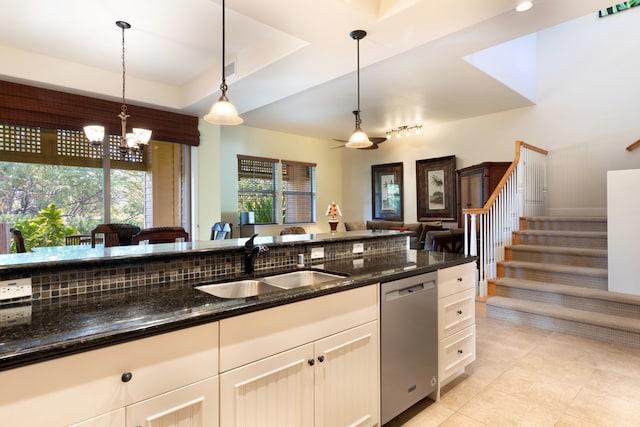 kitchen featuring stainless steel dishwasher, dark stone counters, a tray ceiling, sink, and hanging light fixtures