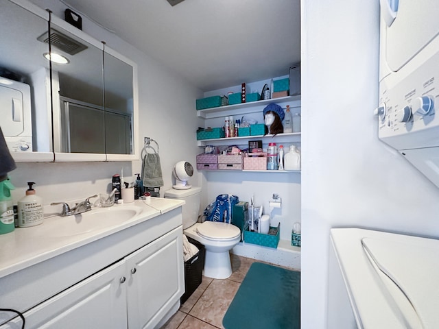 bathroom featuring toilet, a shower with shower door, tile patterned flooring, vanity, and stacked washing maching and dryer