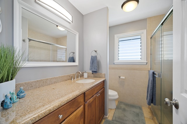 bathroom with vanity, a shower with shower door, tile walls, and toilet