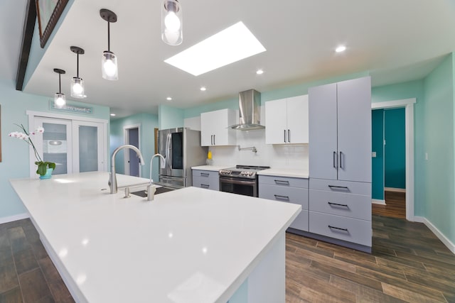 kitchen featuring appliances with stainless steel finishes, wall chimney exhaust hood, an island with sink, and hanging light fixtures