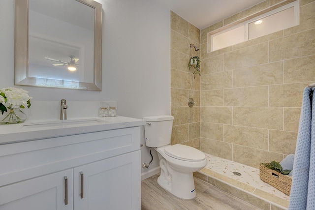 bathroom with a tile shower, vanity, wood-type flooring, and toilet