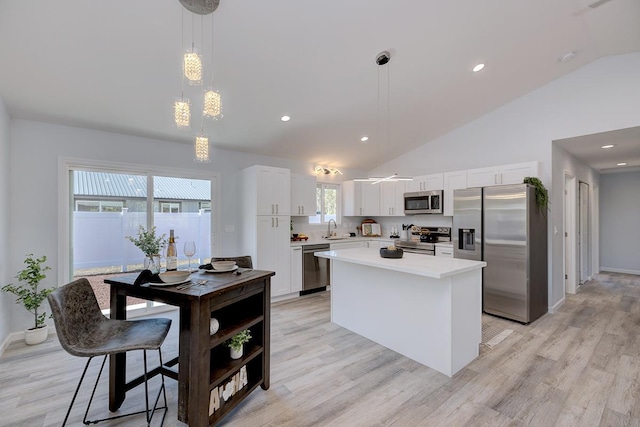 kitchen featuring appliances with stainless steel finishes, light wood-type flooring, decorative light fixtures, white cabinets, and a kitchen island