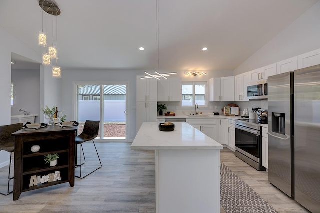 kitchen with white cabinetry, sink, hanging light fixtures, stainless steel appliances, and a kitchen island