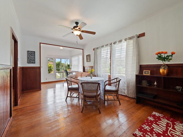 dining area with ceiling fan, wood walls, and wood-type flooring