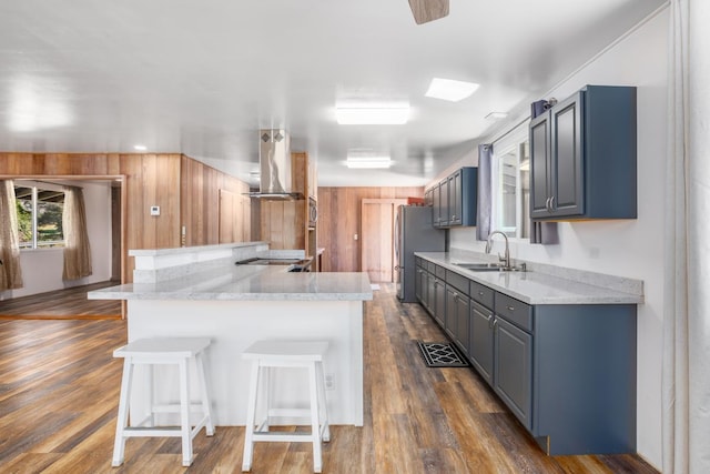 kitchen featuring sink, stainless steel appliances, wall chimney range hood, kitchen peninsula, and a breakfast bar