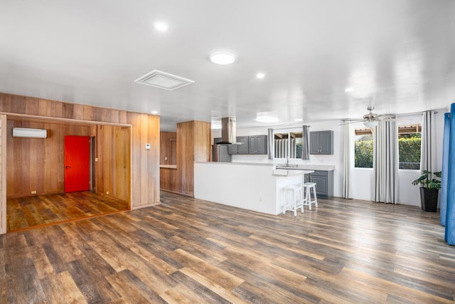 kitchen with dark wood-type flooring, a kitchen breakfast bar, a wall unit AC, gray cabinets, and island range hood