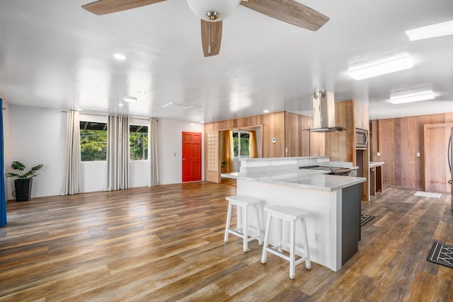 kitchen with island exhaust hood, kitchen peninsula, a breakfast bar, ceiling fan, and stainless steel microwave