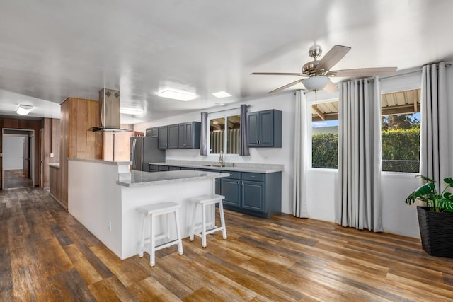 kitchen with ceiling fan, dark hardwood / wood-style floors, stainless steel fridge, island range hood, and a breakfast bar