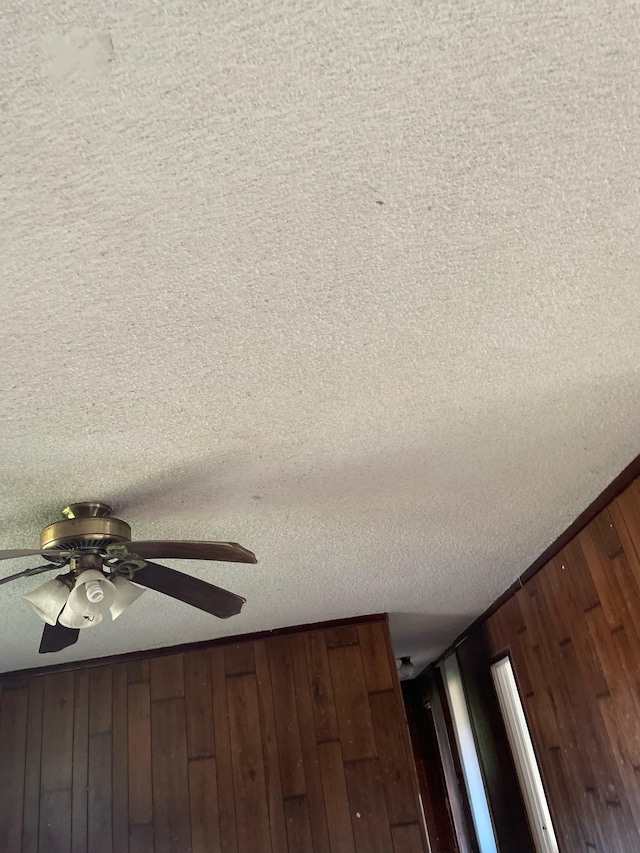 details with ceiling fan, wood walls, and a textured ceiling