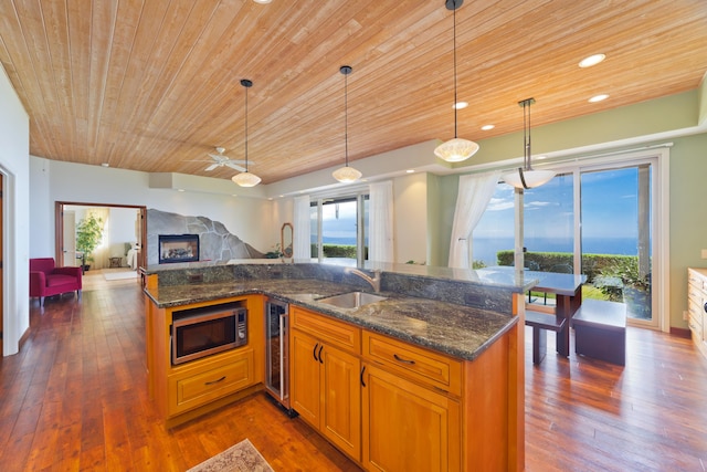 kitchen with wine cooler, pendant lighting, sink, an island with sink, and dark stone counters