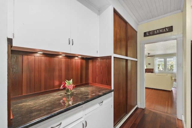 bar with ceiling fan, dark hardwood / wood-style flooring, dark stone countertops, crown molding, and white cabinets