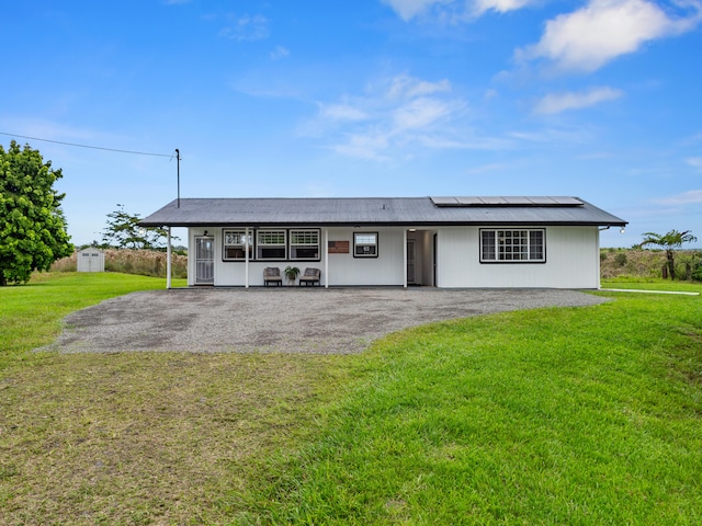 ranch-style house with a front yard, solar panels, and a storage unit