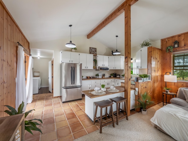 kitchen with appliances with stainless steel finishes, pendant lighting, vaulted ceiling with beams, white cabinetry, and wood walls