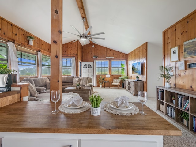 carpeted dining room featuring lofted ceiling with beams, ceiling fan, and wooden walls