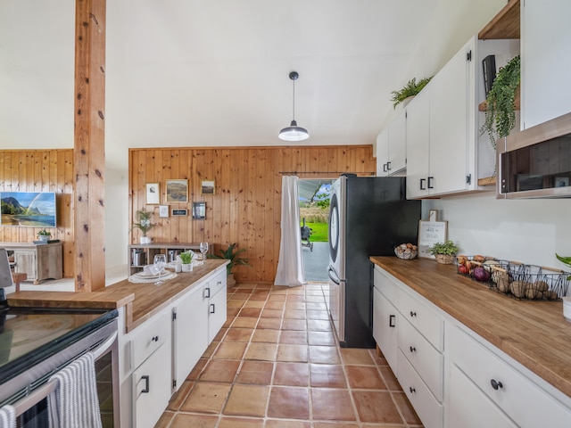 kitchen featuring butcher block countertops, wood walls, decorative light fixtures, white cabinets, and appliances with stainless steel finishes