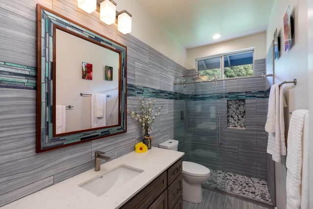 bathroom featuring tiled shower, vanity, toilet, and tile walls