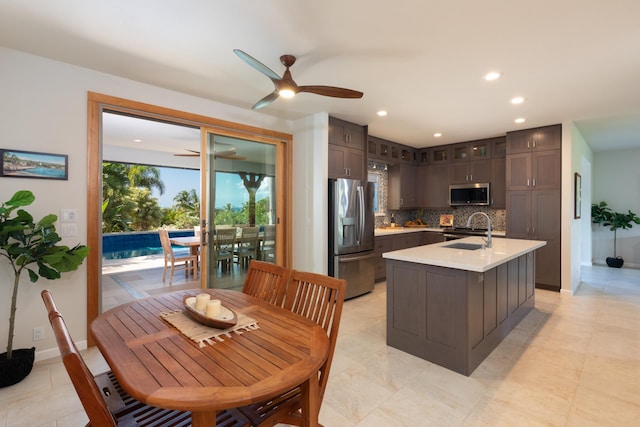 kitchen with appliances with stainless steel finishes, tasteful backsplash, an island with sink, sink, and dark brown cabinetry