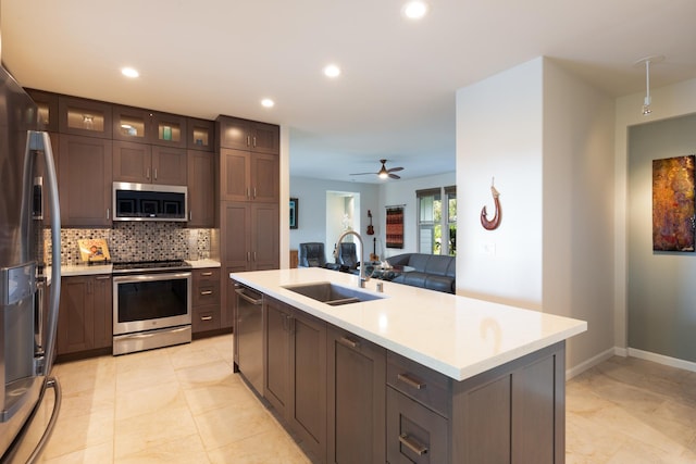 kitchen featuring sink, appliances with stainless steel finishes, tasteful backsplash, dark brown cabinetry, and an island with sink