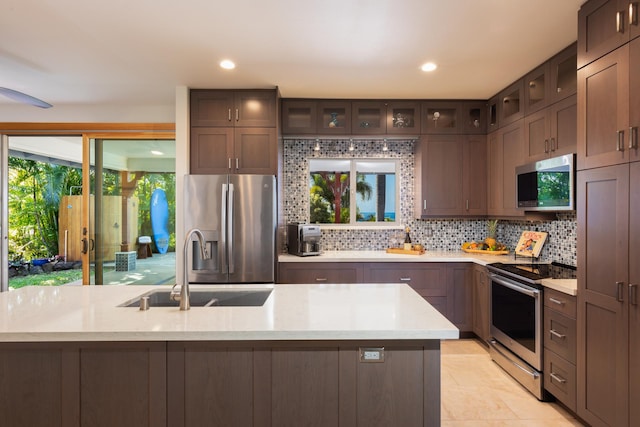 kitchen featuring appliances with stainless steel finishes, sink, decorative backsplash, dark brown cabinets, and a center island with sink