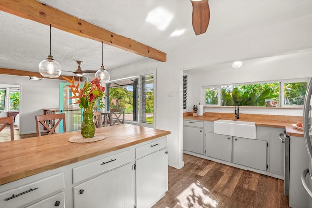 kitchen with butcher block counters, sink, white cabinets, and hanging light fixtures